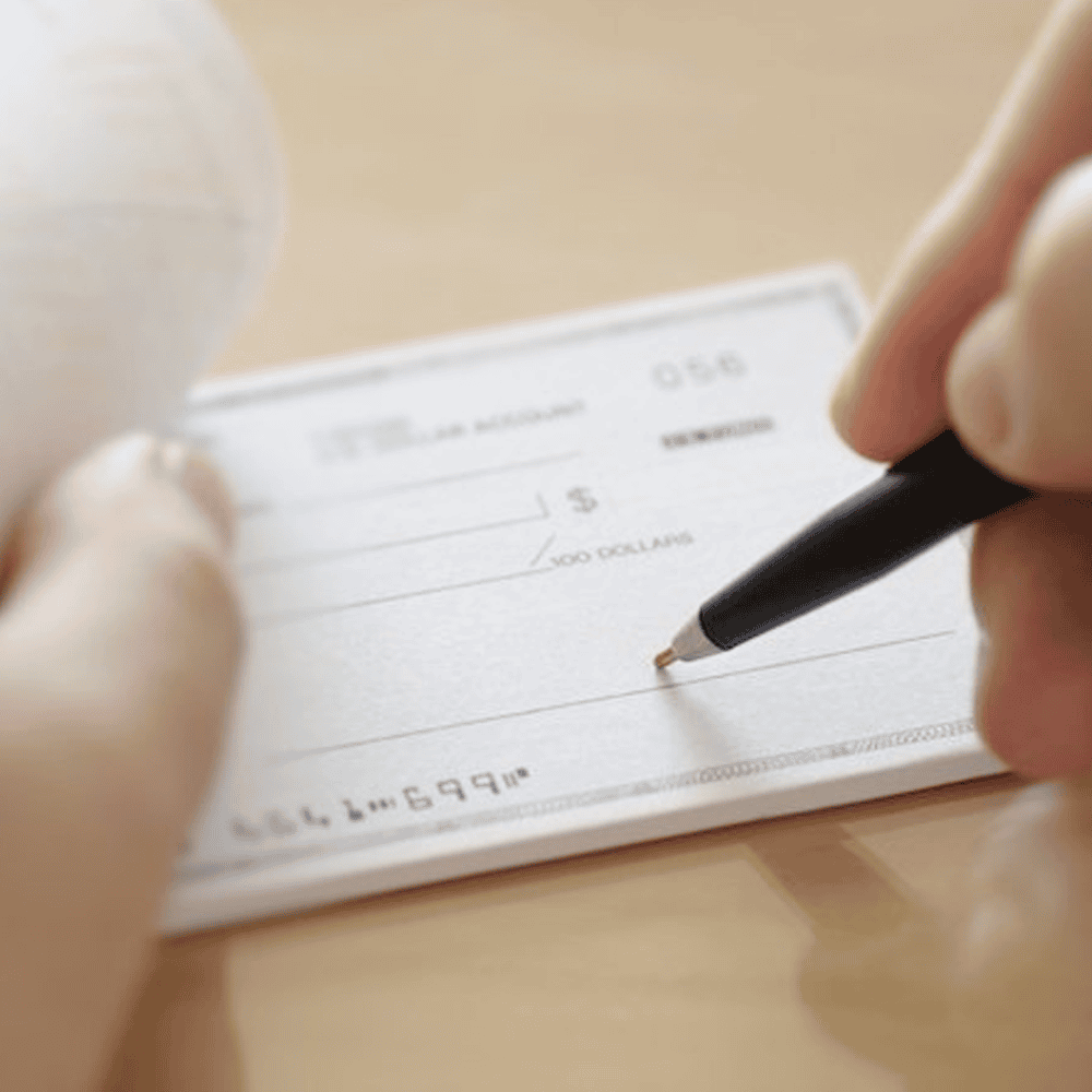check-image Hand writing a check with pen on wooden desk, representing charitable giving and tithing donations